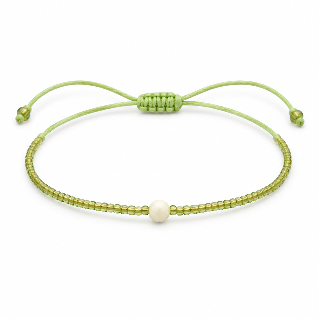 Jasnozielona cienka bransoletka boho z kremowym koralikiem, produkt na bialym tle